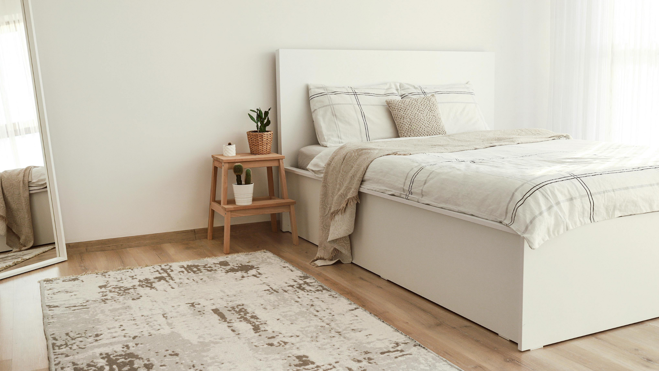 A bedroom with light wood flooring with an abstract patterned rug.
